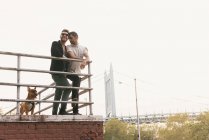 Affettuosa giovane coppia maschile sul lungofiume con cane, Astoria, New York, Stati Uniti d'America — Foto stock