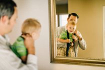 Father putting neck tie on young son, reflected in mirror — Stock Photo
