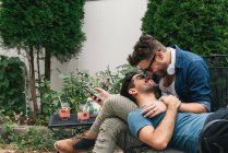 Romântico jovem casal masculino reclinado no jardim, olhando um para o outro — Fotografia de Stock