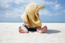 Baby boy playing with mother's sun hat on the beach — Stock Photo