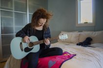 Adolescente tocando la guitarra en el dormitorio - foto de stock