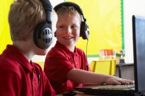 Meninos da escola usando fones de ouvido e olhando para o computador em sala de aula — Fotografia de Stock