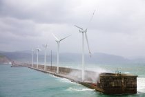 Wind farm on pier with cloudy sky and breaking waves — Stock Photo