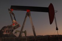 Vista de ángulo bajo de la bomba en el campo de petróleo al atardecer - foto de stock