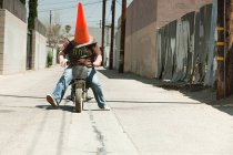 Hombre con cono de tráfico en la cabeza, montar en moto - foto de stock