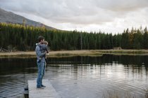 Pai em pé no cais de madeira ao lado do lago, segurando o filho jovem — Fotografia de Stock
