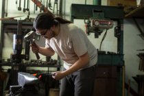 Male metalsmith hammering red hot metal on workshop anvil — Stock Photo