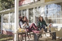 Zwei junge Freundinnen entspannen sich auf der sonnenbeschienenen Terrasse mit Rotwein — Stockfoto