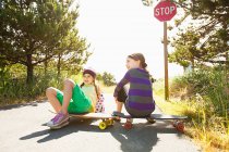 Girls sitting on skateboards along rural road — Stock Photo