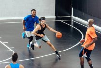 Jugadores de baloncesto masculino corriendo con pelota y defendiendo en cancha de baloncesto - foto de stock