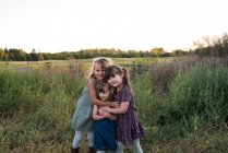 Portrait of three young girls standing together in field, hugging — Stock Photo