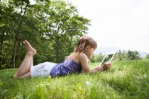 Chica acostada en la hierba con la tableta digital - foto de stock