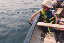 Девушка касается воды с гребной лодки на озере — стоковое фото