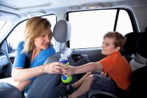 Мать передавала бутылку мальчику на заднем сиденье машины — стоковое фото