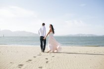 Femme regardant en arrière en se promenant main dans la main avec un copain sur la plage — Photo de stock