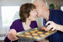 Seniorenpaar küsst sich mit selbst gebackenen Plätzchen — Stockfoto