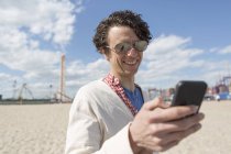 Hombre adulto medio mensajes de texto en el teléfono inteligente en la playa - foto de stock