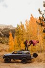 Man shaking sleeping bag on top of vehicle in autumn forest, Mineral King, Sequoia National Park, California, USA — Stock Photo