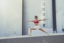 Young woman outdoors, standing on wall in yoga position — Stock Photo