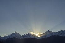 Raios de sol atrás de montanhas cobertas de neve sob o céu azul — Fotografia de Stock