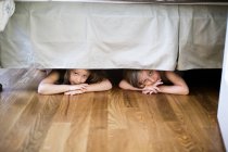 Boy and girl hiding under bed — Stock Photo