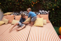 Zwei Jungen spielen auf Gartenmöbeln mit Kissen — Stockfoto