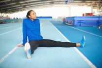 Young female athlete sitting on floor stretching legs — Stock Photo