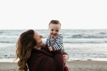 Mãe na praia segurando menino sorridente — Fotografia de Stock
