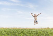 Menino no campo pulando no ar médio — Fotografia de Stock