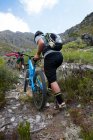 Вид ззаду молода пара штовхає гірські велосипеди вгору по гірській стежці — стокове фото