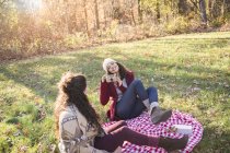Молода жінка на пікніку ковдру фотографує друга — стокове фото