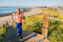 Mujer joven haciendo ejercicio, corriendo escaleras arriba cerca de la playa, vista elevada - foto de stock
