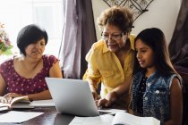 Mother and grandmother helping girl with homework, using laptop — Stock Photo