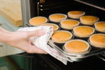 Female hand taking fresh baked muffins from oven — Stock Photo