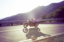 Hombre vestido de rosa onesie, en motocicleta, Malibu Canyon, California, EE.UU. - foto de stock