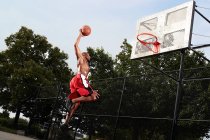 Joven saltando en el aro de baloncesto - foto de stock