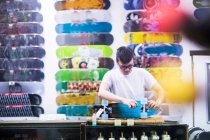 Jeune assistant de vente masculin réparer skateboard au comptoir de magasin de skateboard — Photo de stock