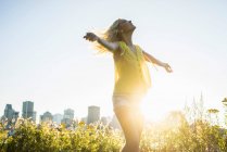 Portrait of beautiful blonde girl dancing with cityscape behind during summer — Stock Photo