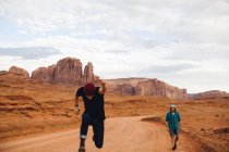 Two men, one sprinting and one walking along dirt track, Monument Valley, Arizona, USA — Stock Photo