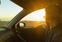 Jeune homme regardant par la fenêtre de la voiture au coucher du soleil — Photo de stock