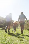 Rear view of mid adult couple and daughter strolling in field — Stock Photo