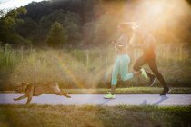 Young couple and dog running in sunlit in park — Stock Photo