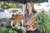 Жінка в фруктовій та овочевій кабінці тримає моркву — стокове фото