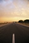 Diminishing view of marked road under sunset cloudy sky — Stock Photo
