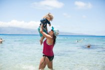 Woman standing in sea, lifting son in air — Stock Photo