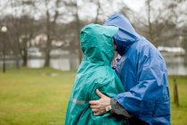Старшая пара в водонепроницаемой одежде целуется в парке — стоковое фото