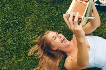 Giovane donna sdraiata sull'erba prendendo selfie con macchina fotografica retrò — Foto stock