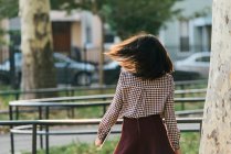 Вид ззаду жінки, що ходить і носить цифровий планшет у міському парку — стокове фото
