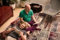 Männliches Paar auf Wohnzimmerboden liest Buch und digitales Tablet — Stockfoto