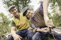 Low angle view of man and boy wearing flat caps whittling twig — Stock Photo